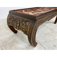 an ornately carved coffee table with carvings on the top and bottom, sitting on a white floor