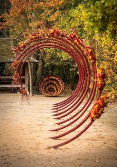 an arch made out of branches and flowers in the middle of a dirt area with benches behind it