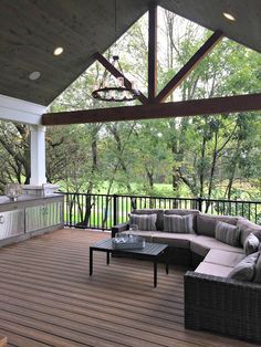 an outdoor living area with couches, tables and grill on the back deck in front of trees