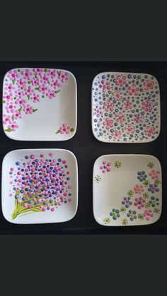 four plates with flowers painted on them sitting in a black box, one is white and the other is pink