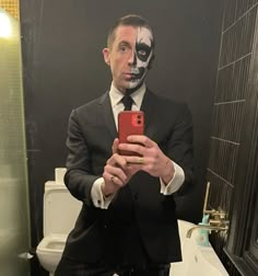 a man in a suit taking a selfie with his cell phone while wearing a mask