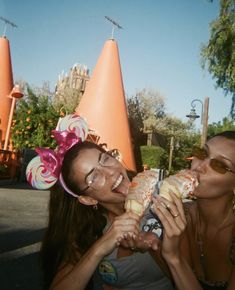 two women eating donuts in front of an orange cone - shaped building at disneyland