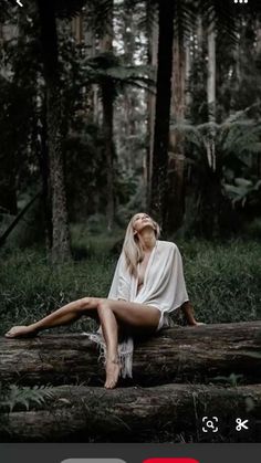 a woman sitting on top of a log in the middle of a forest next to trees