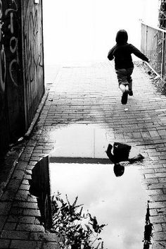 a child jumping into a puddle in the street