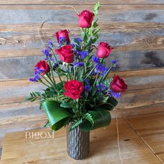 a vase filled with red roses and purple flowers on top of a wooden table next to a wall