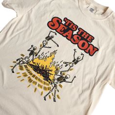 Get into the spirit of spookiness with our 'Tis The Season - Vintage Halloween T-Shirt! This one-of-a-kind, retro-inspired tee is perfect for those who love Halloween and autumn. The quirky graphic showcases a gang of skeleton pals boogying around a campfire. Our creative artists crafted this as a throwback to 1970's style, delivering a truly original shirt design. Indulge in unmatched comfort and style with our handcrafted t-shirts, featuring playful and unique designs. Proudly created in Penns 1970s Graphic Tee, Halloween Band Merch T-shirt With Graphic Design, Vintage Graphic Print T-shirt For Fall, Fall Graphic Crew Neck T-shirt, Fall Graphic Design Crew Neck T-shirt, Pop Culture Screen Print Tops For Fall, Retro Fall T-shirt With Screen Print, Fall Fan Apparel T-shirt With Graphic Print, Vintage Halloween Fan Merchandise T-shirt