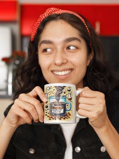 a woman holding up a coffee mug in front of her face and smiling at the camera