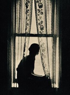 the silhouette of a woman sitting in front of a window with curtains on both sides