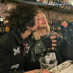 two people sitting at a table with drinks in front of them, one kissing the other