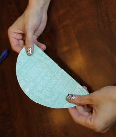 two hands holding a piece of paper with writing on it and scissors in the background