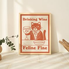 a poster with a cat drinking wine next to a potted plant on a table