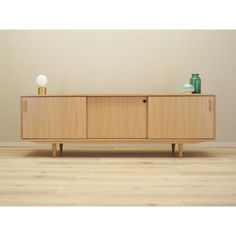 an empty room with a wooden cabinet and vases on the sideboard, against a beige wall