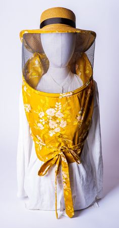 a mannequin's head wearing a yellow dress with flowers and mesh covering it