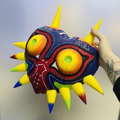 a person holding up a colorful mask with spikes on it's face and eyes