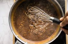 a person is stirring some food in a pot on the stove top with a whisk