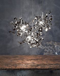 a chandelier hanging from the ceiling over a wooden table in front of a black wall