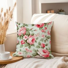 a flowered pillow sitting on top of a couch next to a cup