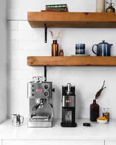 a coffee maker sitting on top of a white counter next to shelves filled with cups