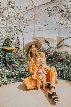 a woman sitting on the ground holding a baby in her lap and wearing a hat