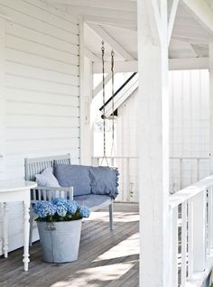 a white porch with blue flowers in a pot and a bench on the front porch