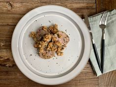 a white plate topped with meat next to a fork and knife on top of a wooden table