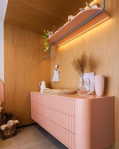 a pink dresser in a room with wood paneling on the walls and shelves above it