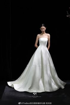 a woman in a white wedding dress standing on a black background with her hands behind her back