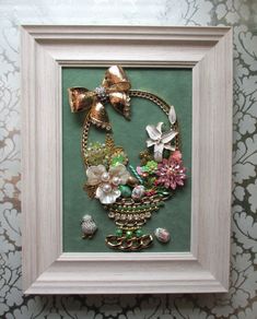 a white frame holding a painting with flowers and other things in it on a wall