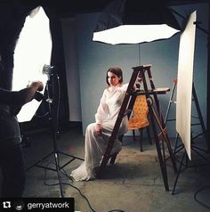 a woman is sitting on a ladder in front of a camera and light set up