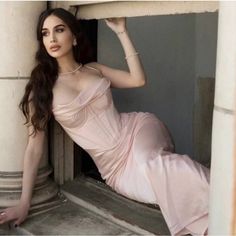 a woman in a pink dress leaning against a pillar with her hand on the wall