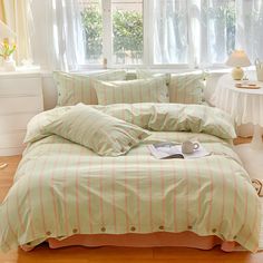 a bed with green and pink striped comforter next to a white table in front of a window