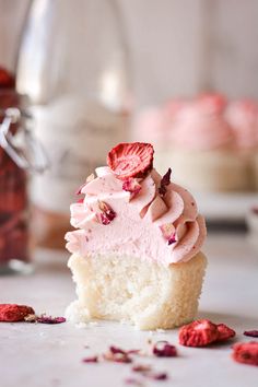 a cupcake with pink frosting and strawberries on the top is half eaten