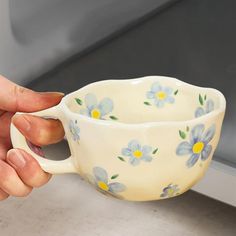 a hand holding a cup with blue flowers on it