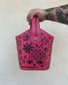 a hand holding a pink bag with black designs on it and tattoos on the arm