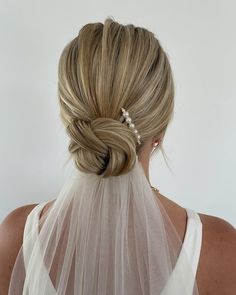 a woman with blonde hair wearing a white veil and pearls in her hair is seen from the back