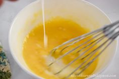 a white bowl filled with yellow liquid and whisk