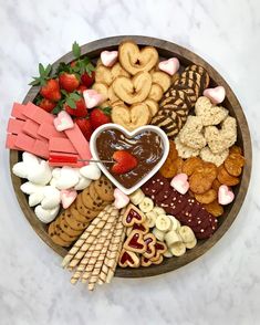 a wooden platter filled with heart shaped cookies, pretzels, strawberries and other snacks