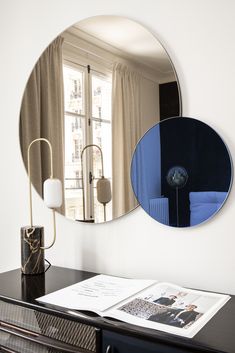 a mirror on the wall above a dresser with a lamp and magazine in front of it