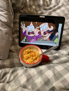 a bowl of cereal is sitting on the bed with an ipad in front of it