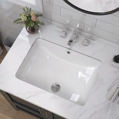 a white sink sitting under a bathroom mirror next to a counter top with a potted plant on it