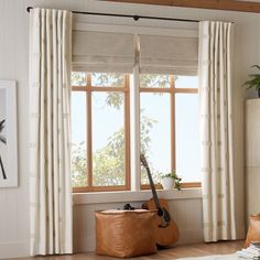 a guitar sits on the floor in front of a window with drapes and curtains