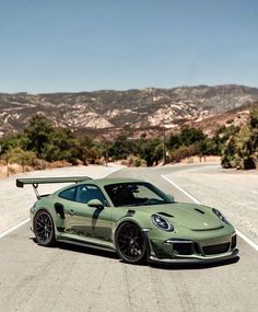 a green sports car parked in the middle of an empty road with mountains in the background