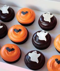 cupcakes decorated with orange frosting and black icing in a box