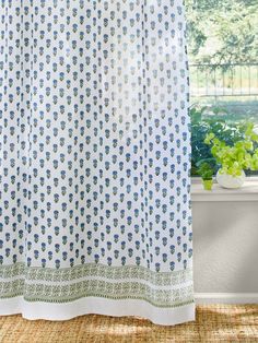 a white curtain with blue and green flowers on it in front of a window sill