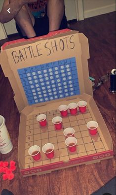 a man sitting on the floor next to a board game with cups in front of it