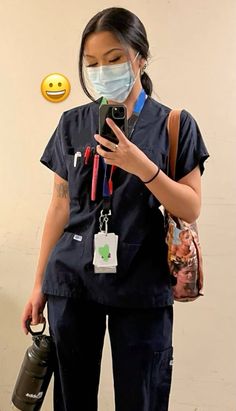 a woman in scrubs is looking at her cell phone while wearing a face mask