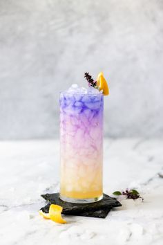 a tall purple and yellow drink sitting on top of a white table next to lemon wedges