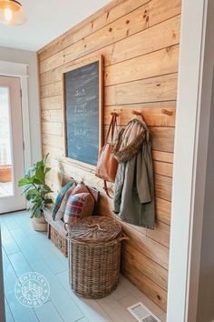 a wooden wall with a chalkboard and coat rack on the side, next to a wicker basket filled with purses