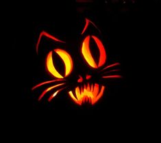 a pumpkin carved to look like a cat's face with glowing eyes and fangs