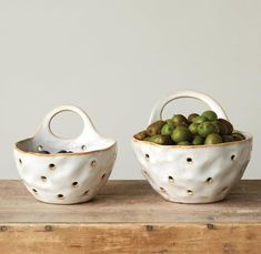 two white bowls filled with green olives sitting on top of a wooden table next to each other